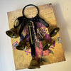 A set of decorative metal wind chimes hanging from a black leather strap on aged paper.