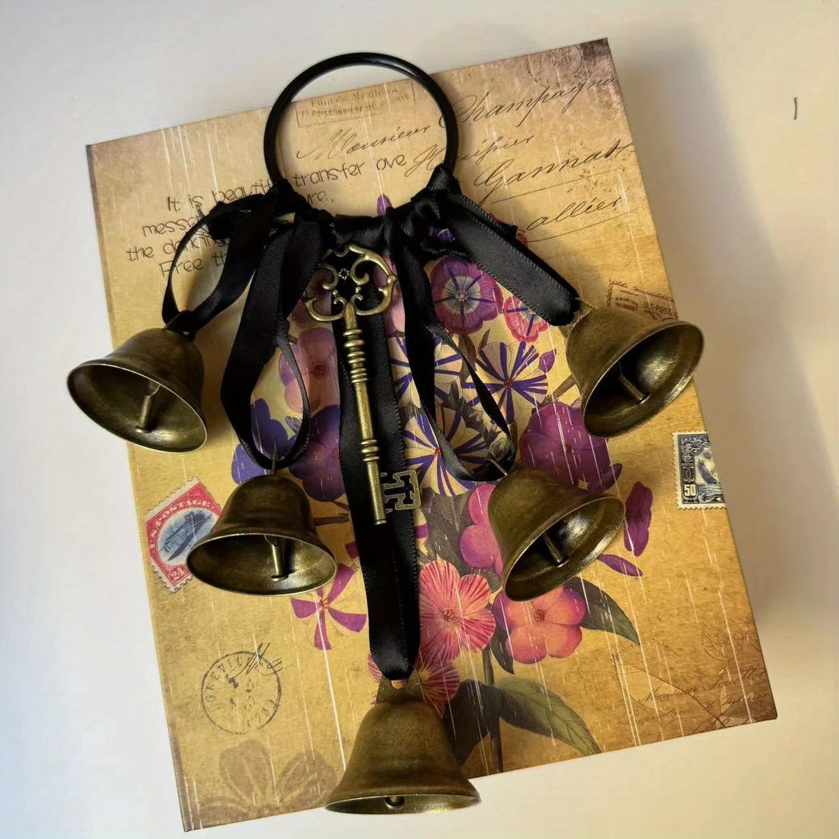 A set of decorative metal wind chimes hanging from a black leather strap on aged paper.