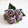 A bouquet of purple silk rose and peony artificial flowers with green leaves.