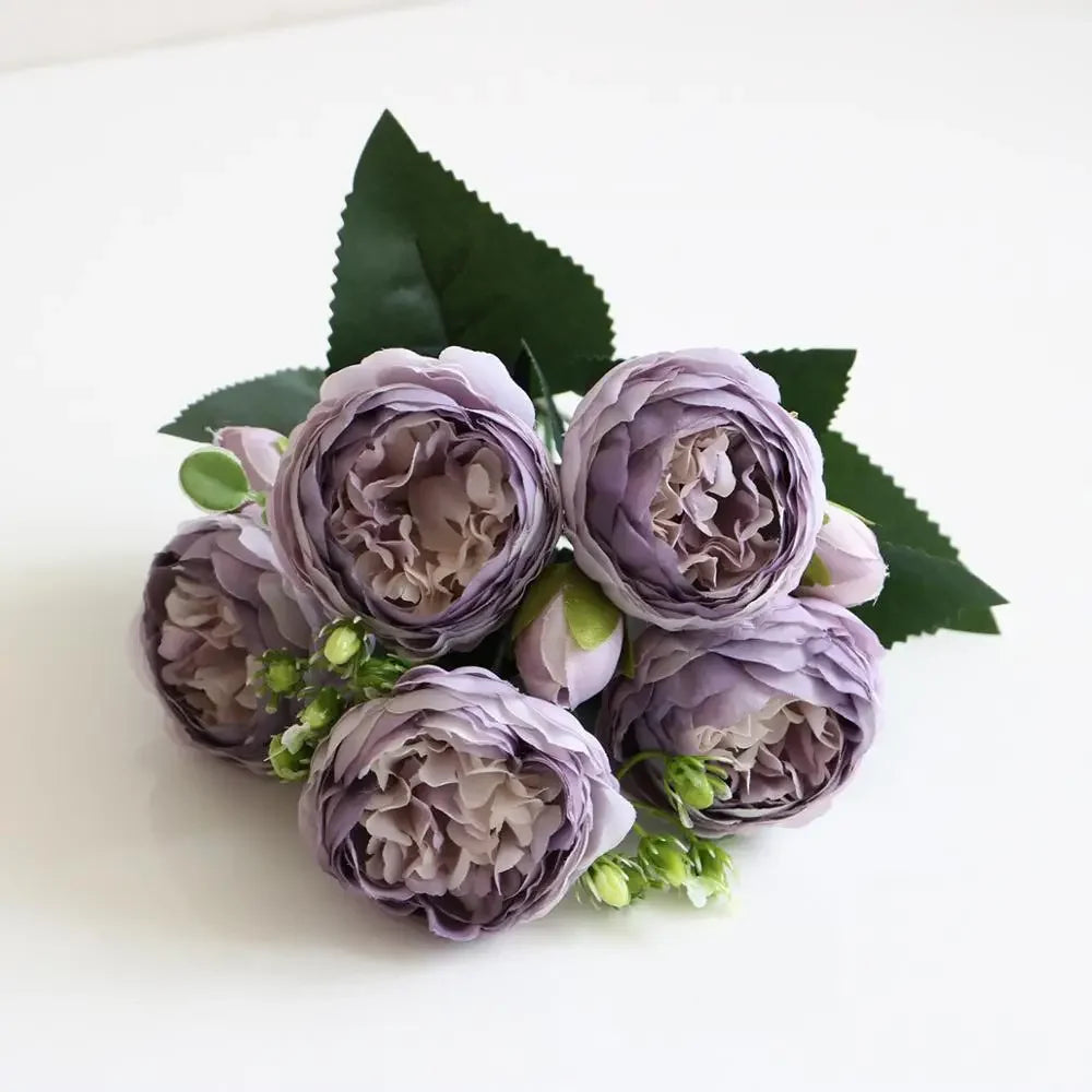 A bouquet of purple silk rose and peony artificial flowers with green leaves.