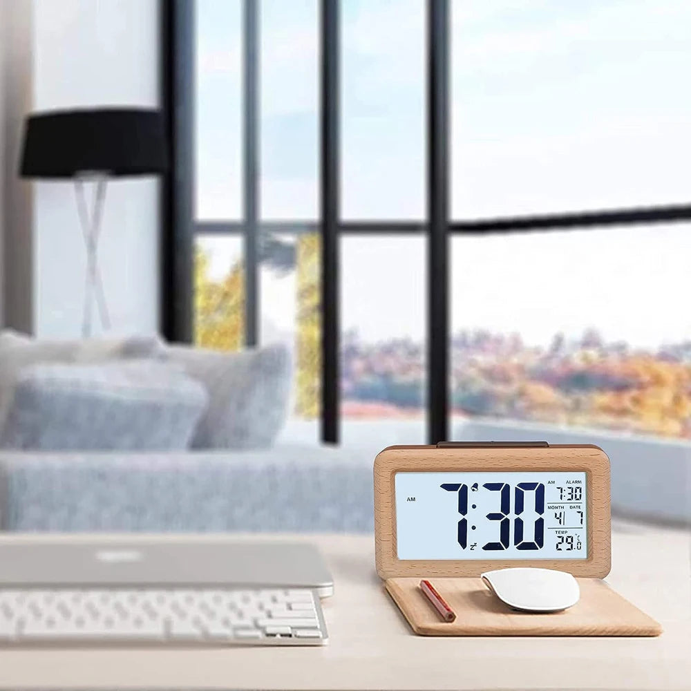 A solid wood digital alarm clock displaying 7:30, with a calendar and temperature display, resting on a desk next to a laptop