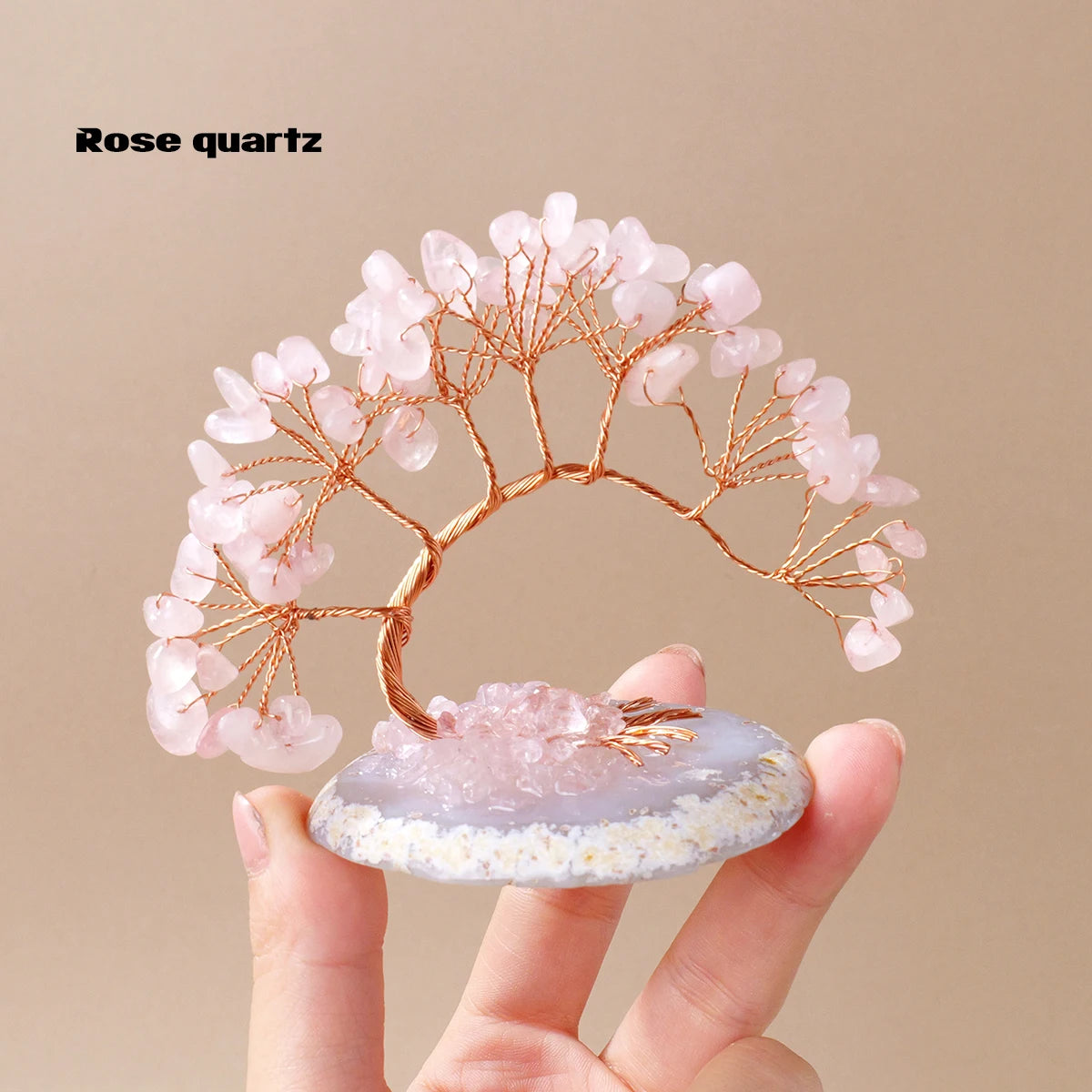A delicate rose quartz crystal tree with pink blossoms stands on a translucent agate base.