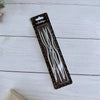 A package of long thin birthday candles with spiral tips displayed on a white wooden surface.