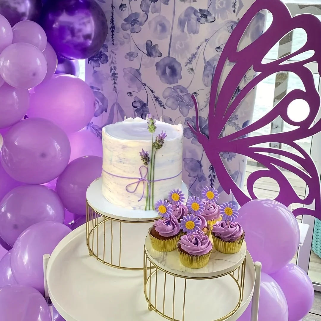 A tiered cake display featuring purple and white balloons, set against a backdrop of purple floral wallpaper and a large purp