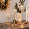 A set of elegant gold metal glass candle holders decorated with pine branches and natural elements.
