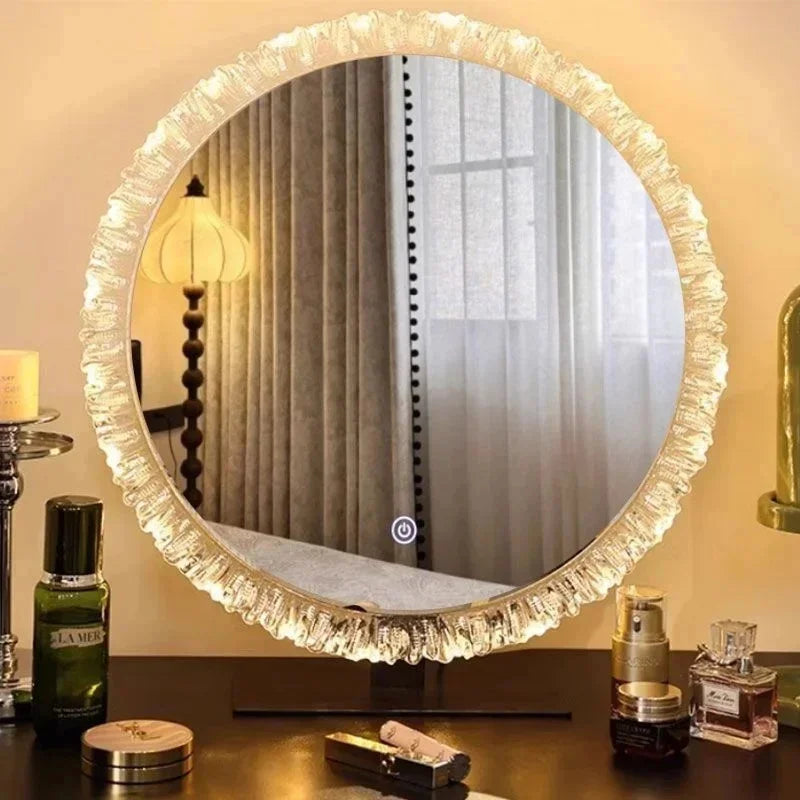 A round, ornate gold-rimmed vanity mirror reflects a room with light curtains and a lamp.