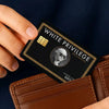 A hand holds a black credit card with gold accents and text, resting on a brown leather wallet.
