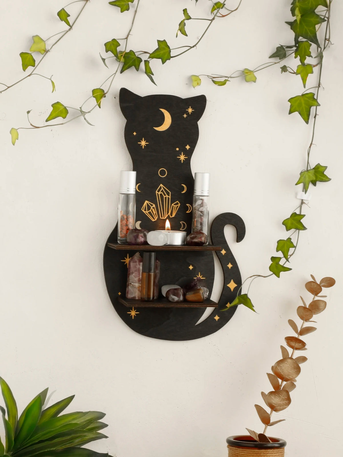 A black cat silhouette with a crescent moon design holds various crystals and glass bottles on a floating shelf.