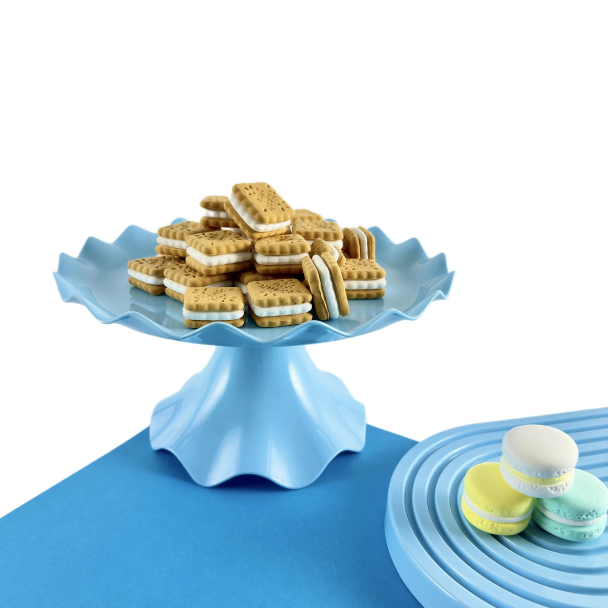 A light blue plastic cake stand holding several rectangular sandwich cookies on a blue surface.