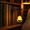 A vintage bookshelf lantern lamp with a carved face hangs on a wooden shelf among old books.