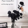 A hand arranges a bouquet of artificial black roses in a glass vase on a white mantelpiece.