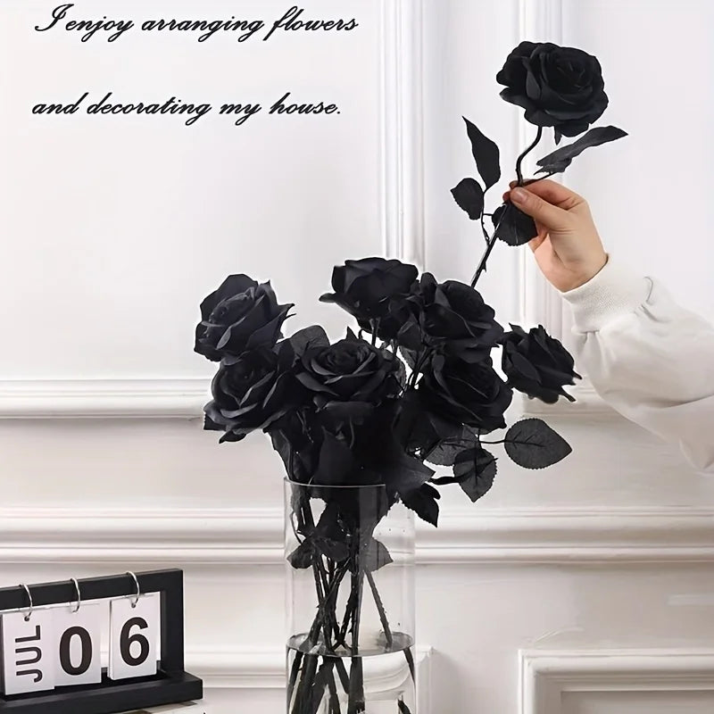 A hand arranges a bouquet of artificial black roses in a glass vase on a white mantelpiece.