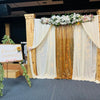 An elegant rectangular backdrop featuring sheer white drapes and gold fringe for an event setting.