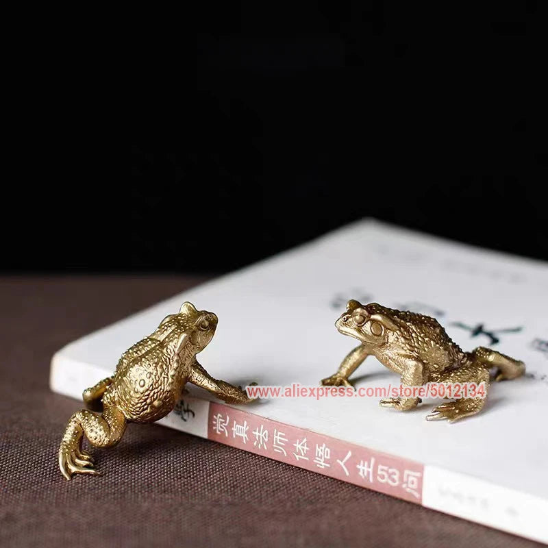 A brass money frog feng shui figurine resting on a book.