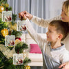 A young child is hanging an acrylic Christmas cash gift ornament with a velvet ribbon on a decorated Christmas tree.