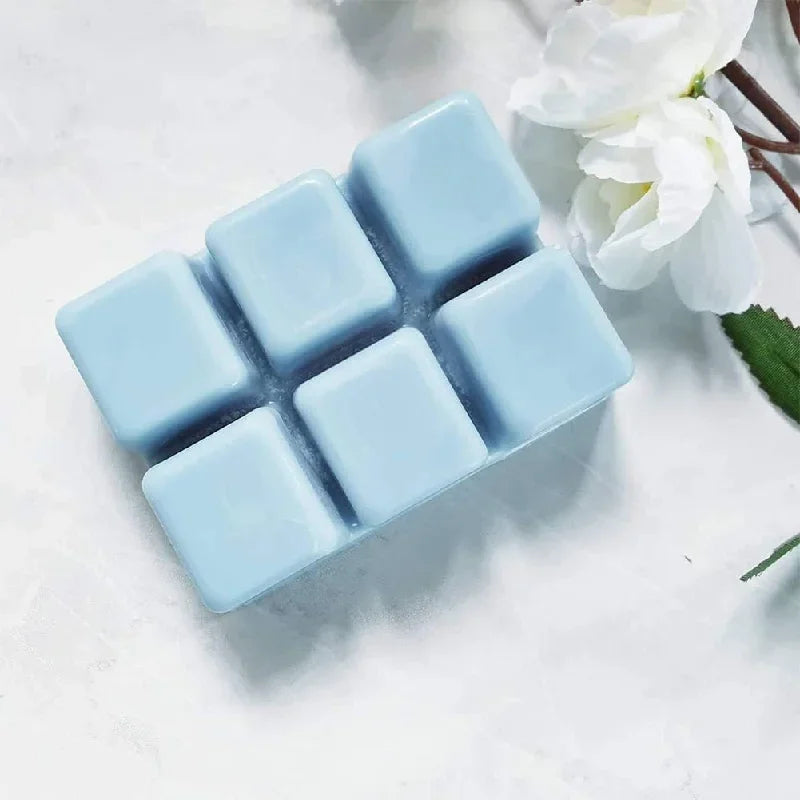 A silicone plastic clamshell mold with six square cavities for DIY wax melts, resting on a white surface next to a white flow