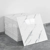 A stack of white faux marble peel-and-stick wall tiles with gray veining displayed on a gray floor.