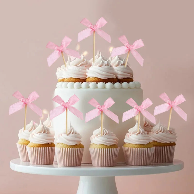 A tiered white cake decorated with pink buttercream frosting and pink bow toppers on a white stand.