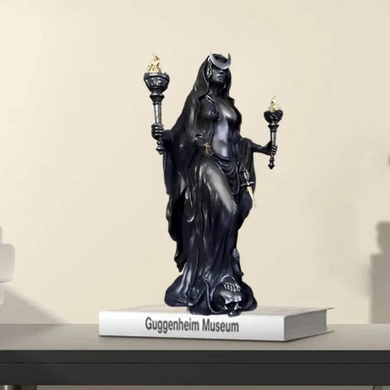 A dark resin statue of a goddess with a crown and mystical details standing on a book.