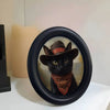 A black cat portrait in a wooden photo frame with a reddish scarf, set against a light background.