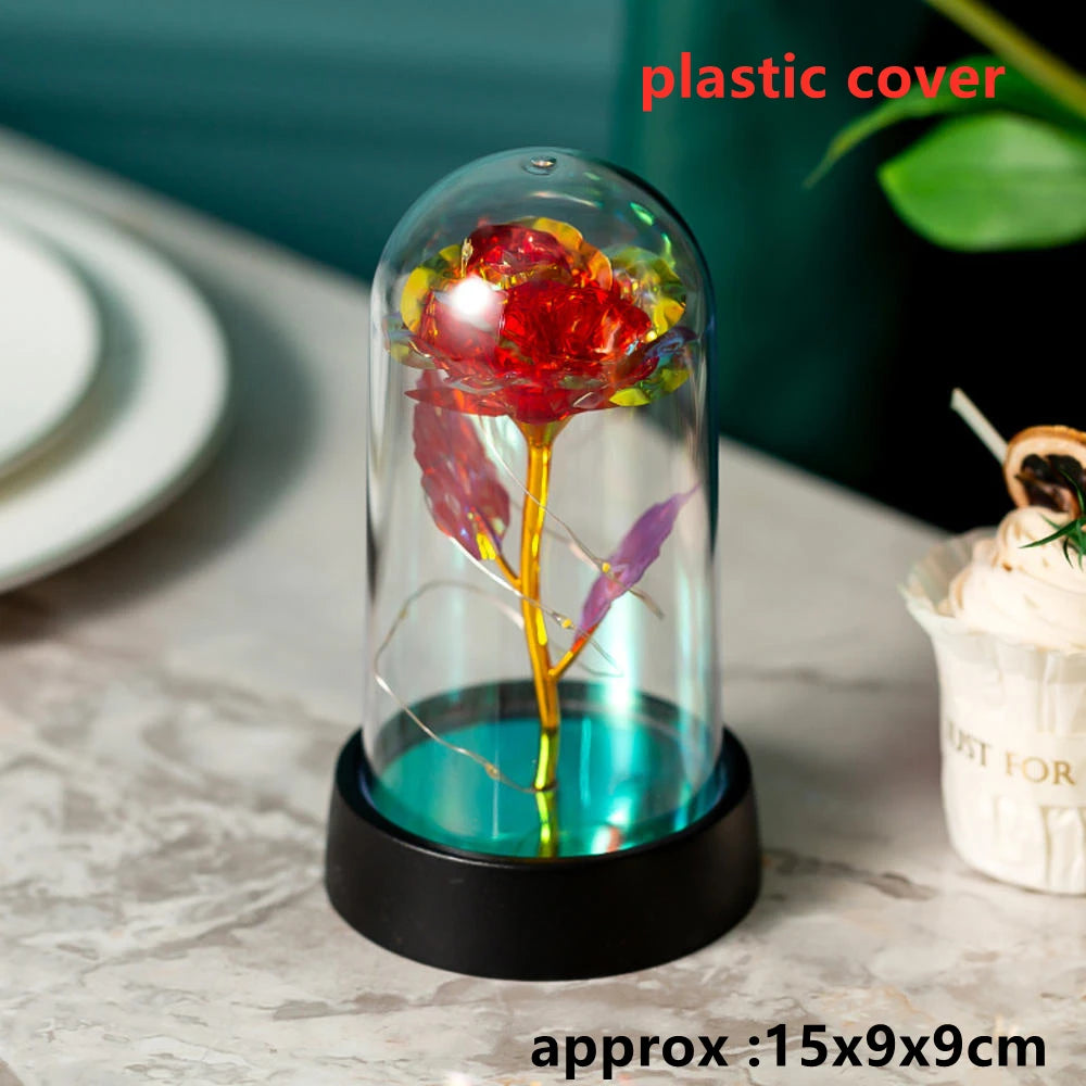 A glass dome containing an artificial red rose flower illuminated by an LED light on a black base.