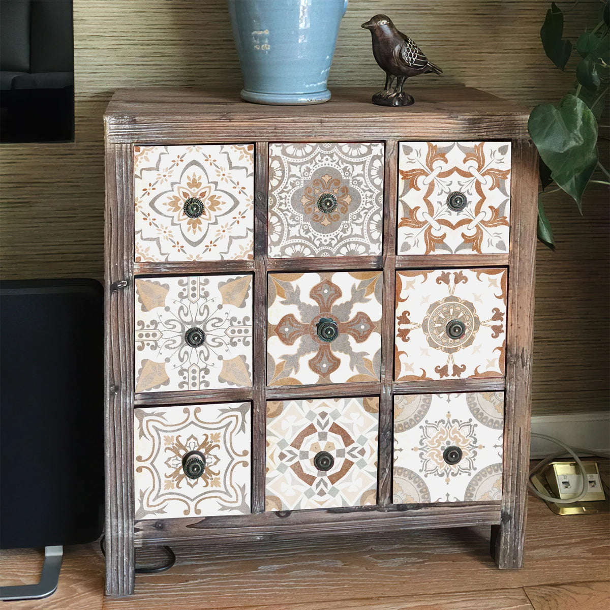 A wooden cabinet displaying square self-adhesive tile wall stickers in beige and brown tones.
