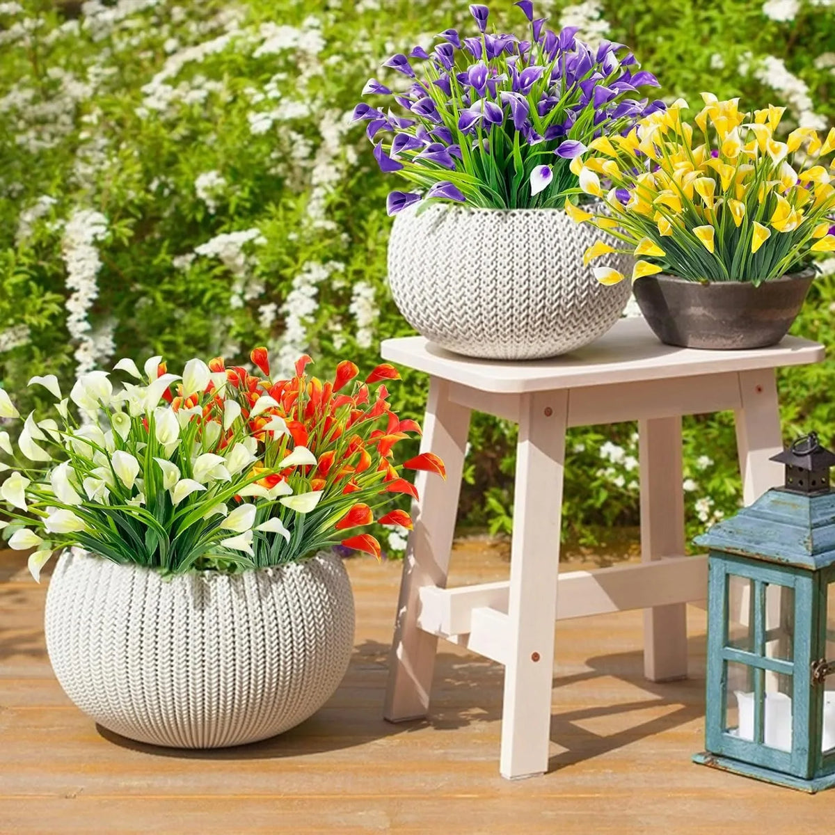 A display of artificial calla lily bouquets in purple, yellow, and red flowers potted in white textured ceramic on a wooden t