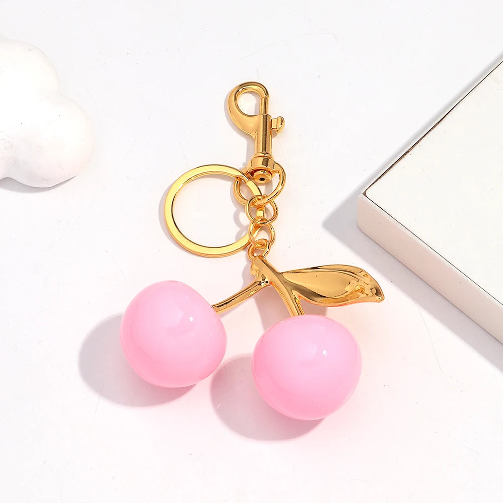 A gold-colored resin pendant keychain featuring a pink cherry bead and a leaf charm.