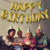 A group of people celebrating a birthday with a banner made of gold foil balloons.