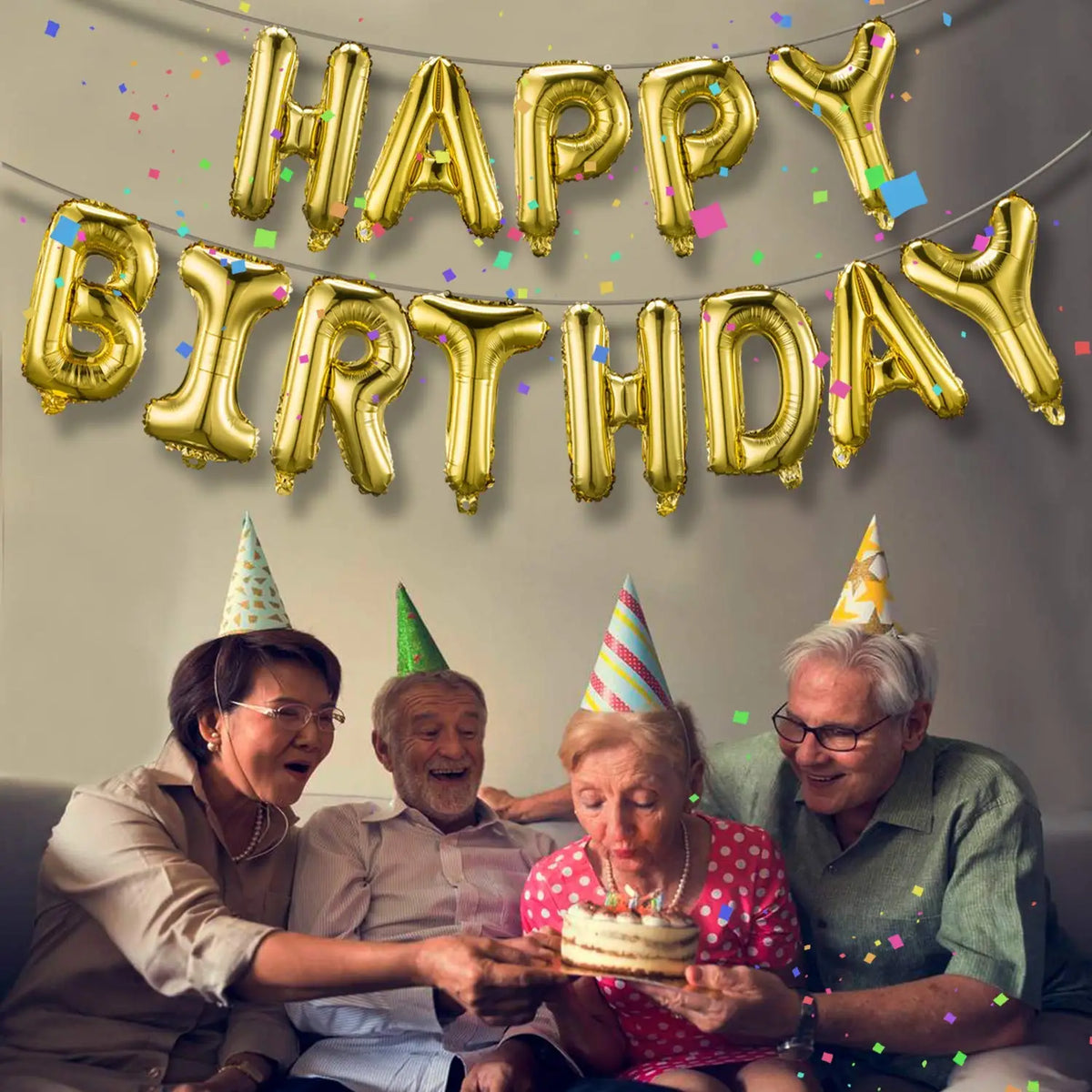 A group of people celebrating a birthday with a banner made of gold foil balloons.