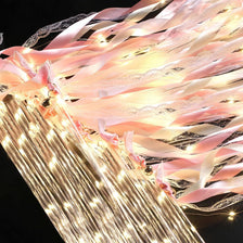 Golden LED glow wands with pink ribbons and bells creating a sparkling light effect