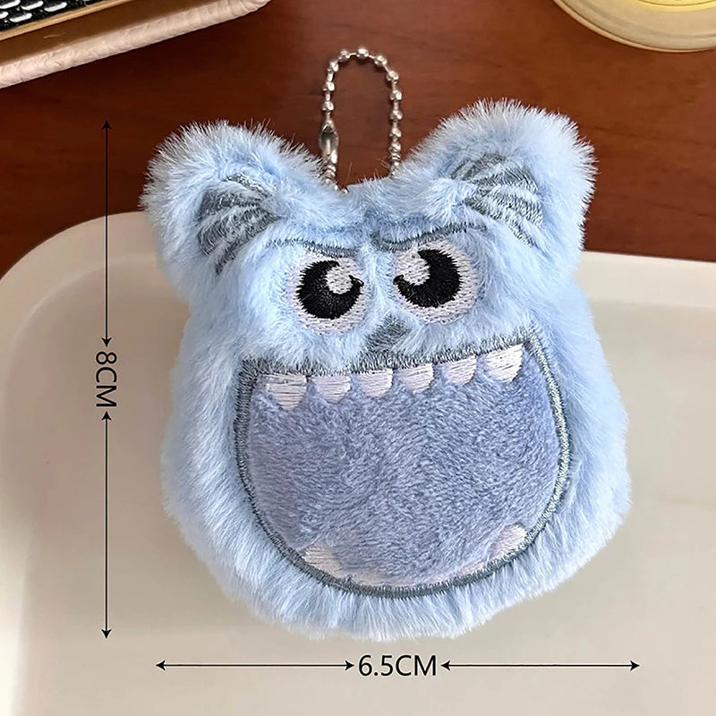 A light blue fuzzy plush monster keychain with large eyes and a wide mouth.
