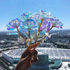 A hand holds a bouquet of iridescent, rainbow-colored artificial crystal flowers against an urban skyline backdrop.