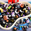 A bowl filled with black resin flatback Halloween charms featuring pumpkin and ghost embellishments.