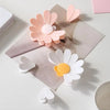 Clips magnéticos de margarita rosa y blanca dispuestos sobre una superficie clara con papel kraft.