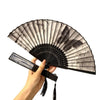 A hand is opening an antique style bamboo folding hand fan with black and white patterns.