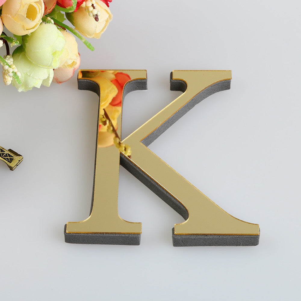 A gold letter K cutout for a mirror wall decal set resting on a white surface with floral elements.