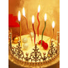 A golden birthday cake decorated with a crown of pearls and lit candles topped with star-shaped flames.