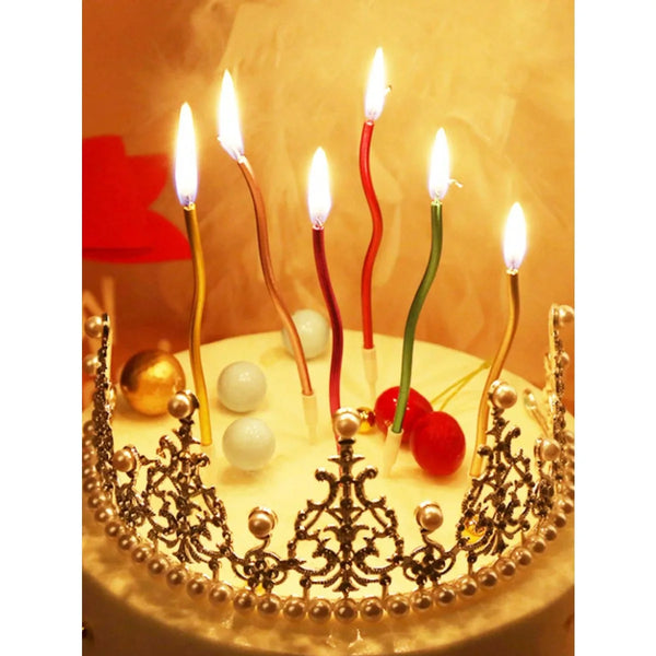 A golden birthday cake decorated with a crown of pearls and lit candles topped with star-shaped flames.