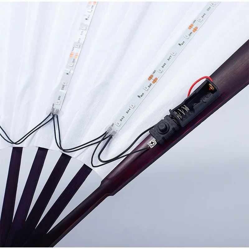 An illuminated folding hand fan with LED lights is shown open, displaying the light strip and fan blades.
