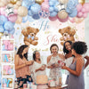 A group of people celebrating a gender reveal with a balloon arch featuring pink, blue, gold, and nude balloons.