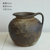 A dark, textured ceramic pitcher or vase with a handle and spout is shown against a light background.