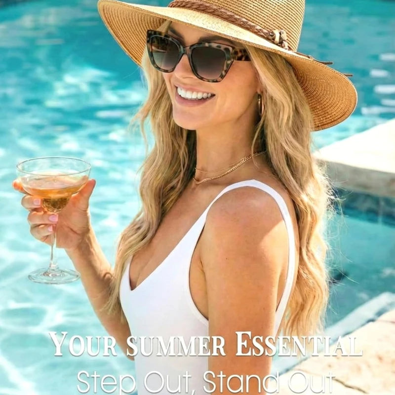 A blonde woman wearing sunglasses and a wide brim straw hat smiles while holding a glass of iced tea near a swimming pool.
