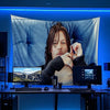 A man with long hair is holding a blue American flag banner in front of a computer monitor.
