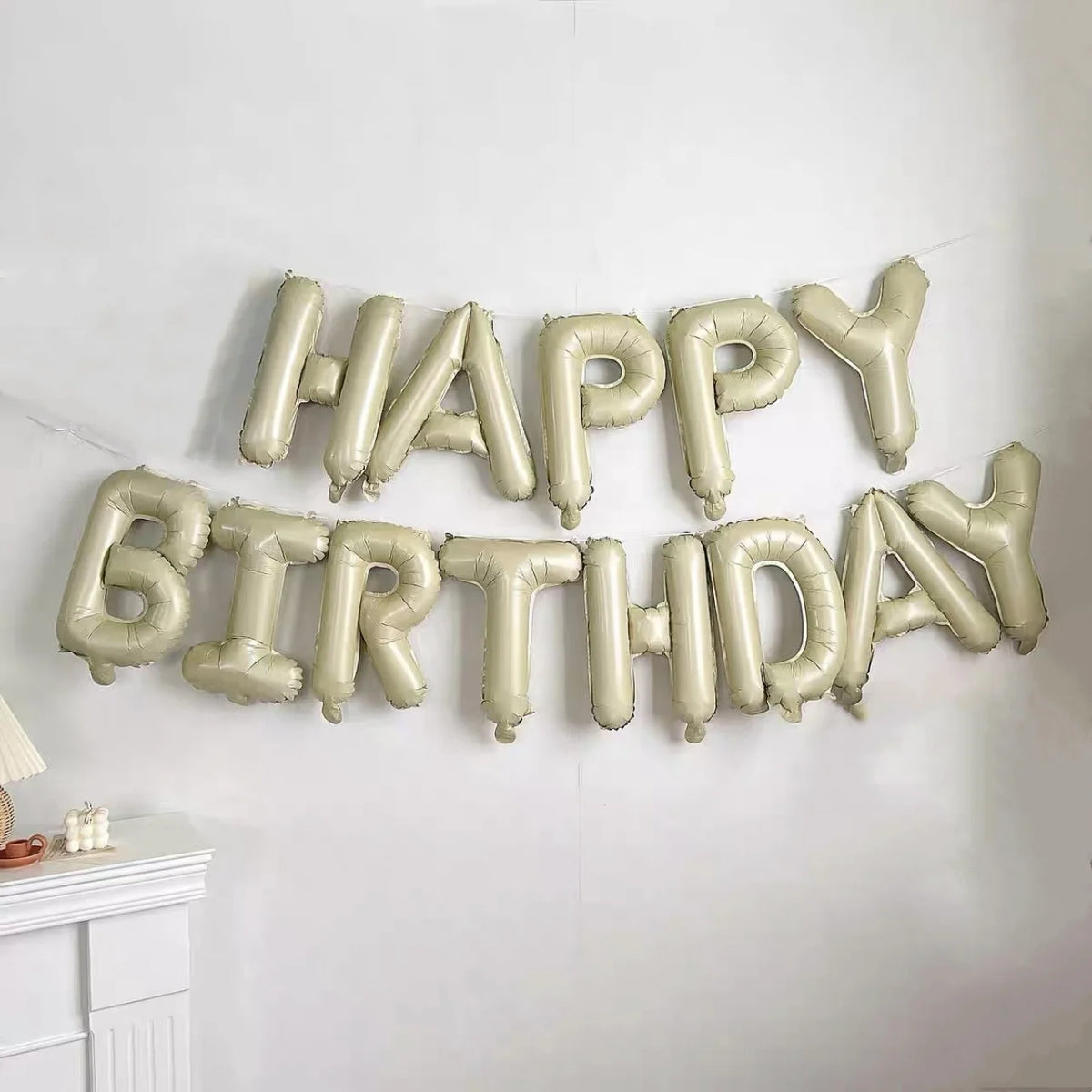 A banner spelling out Happy Birthday made of silver foil letter balloons on a white wall.