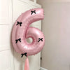 A large pink foil balloon shaped like the number six with black bows, hanging on a white door frame.