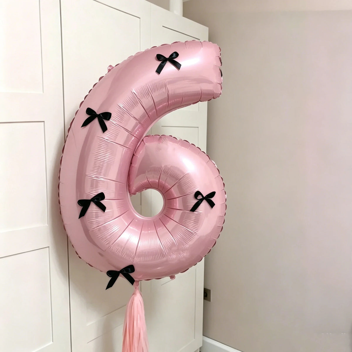 A large pink foil balloon shaped like the number six with black bows, hanging on a white door frame.