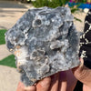 A hand holds a rough, translucent gray and white natural zinc crystal cluster.