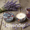 A small candle in a glass holder surrounded by lavender flowers and a tin labeled lavender.