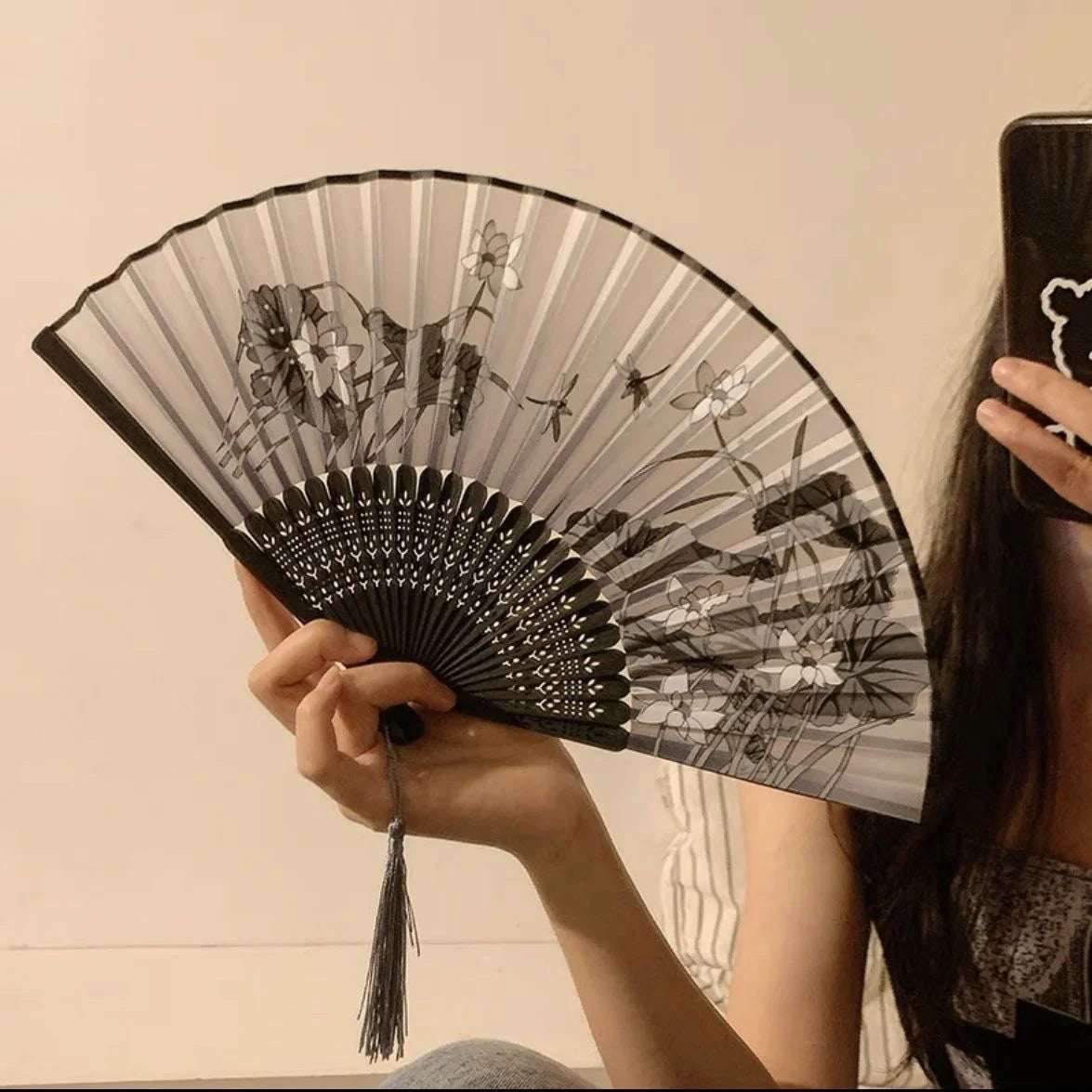 A black and white antique style bamboo folding hand fan is held by a person against a light background.